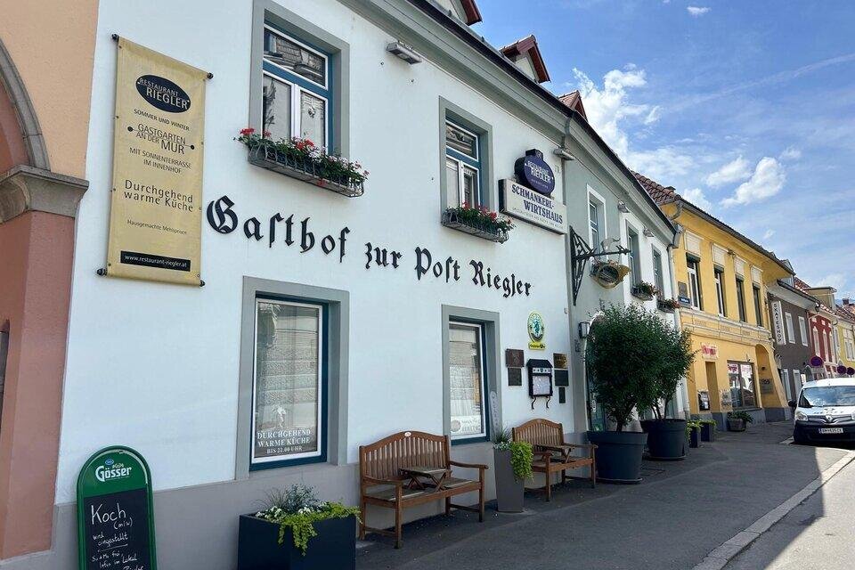 Ein älteres Gasthaus mit dem Namen "Gasthof zur Post Riegler" in einer malerischen Straße. Die Fassade ist hell gestrichen und mit Blumen in Fensterkästen geschmückt. | © TV Hochsteiermark