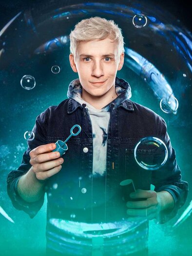 Ein junger Mann mit blonden Haaren lächelt freundlich in die Kamera. Der Hintergrund zeigt eine farbenfrohe, abstrakte Darstellung mit Blasen. | © Mellow