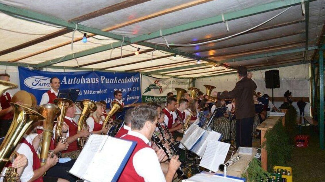 Eine Blaskapelle spielt in einem Festzelt. Die Musiker tragen traditionelle Kleidung und sind umgeben von Instrumenten. | © FF Zauchen