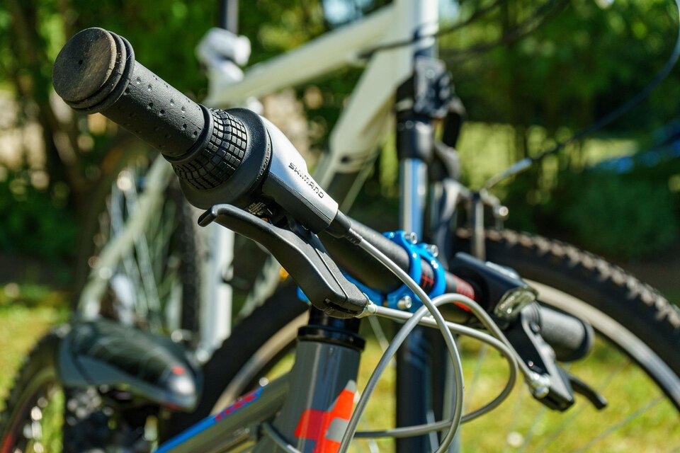Ein Nahaufnahme von einem Fahrradlenker mit Schaltungen. Im Hintergrund sieht man den Rahmen eines weiteren Fahrrads und grünes Gras. | © Pixabay