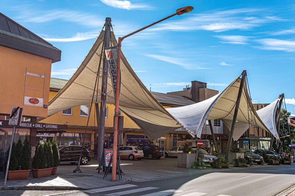 Ein moderner Marktplatz mit schattenspendenden Stoffdächern. Die Umgebung ist hell und freundlich, ideal für einen Einkaufsbummel. | © Platzlmarkt
