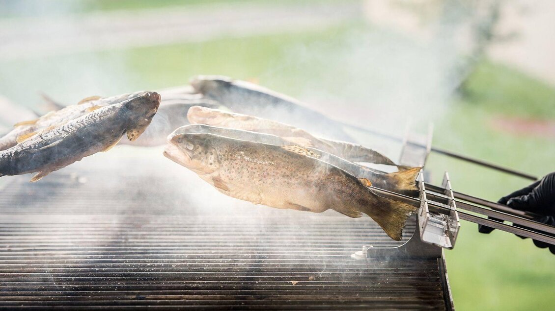 Frisch gegrillter Fisch auf einem Grill. Rauch steigt auf, während der Fisch mit einer Grillgabel gewendet wird. | © Tauroa