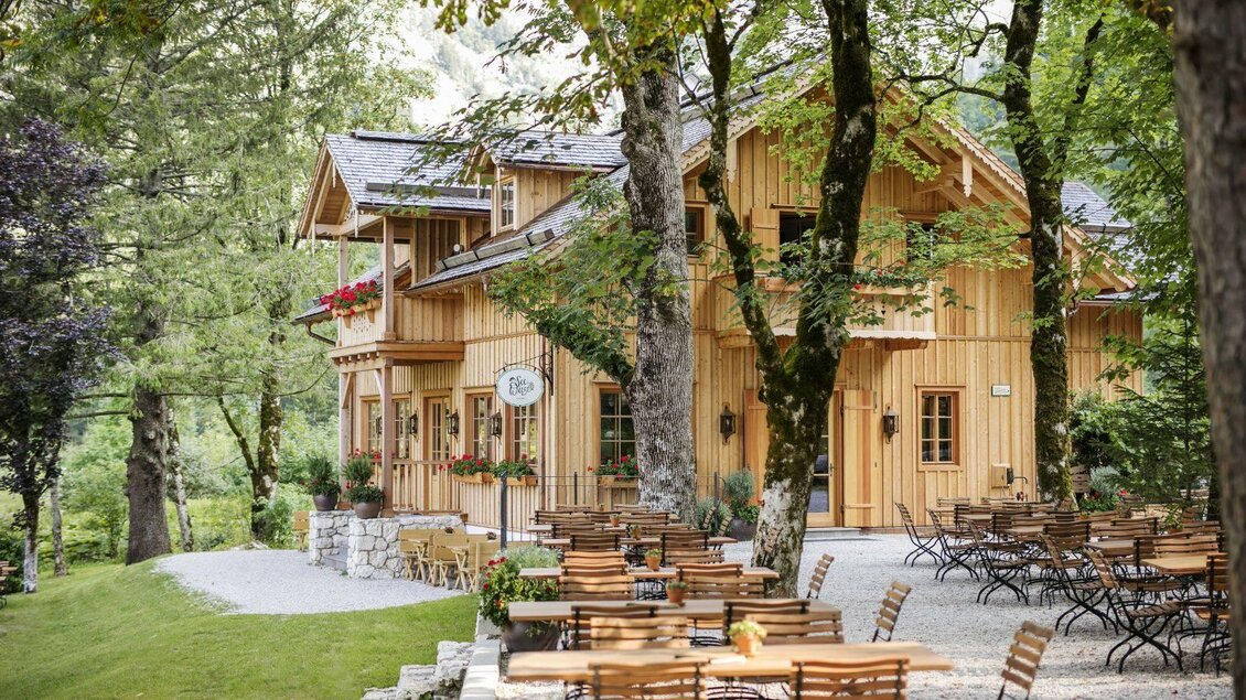 Ein gemütliches Holzhaus umgeben von Bäumen. Draußen stehen Terrassen mit Tischen und Stühlen. | © Tauroa