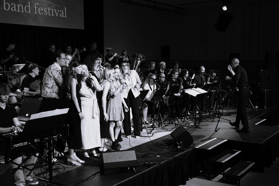 Eine Gruppe von Sängern steht auf der Bühne und gibt ein Konzert. Im Hintergrund ist ein Orchester zu sehen, das die Darbietung begleitet. | © Zehnerhaus