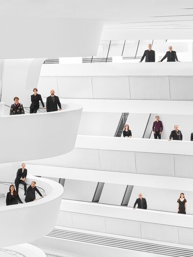A modern, bright architecture with multiple levels. People are standing on the balustrades and in various positions in the room. | © _c__Tina_Herz