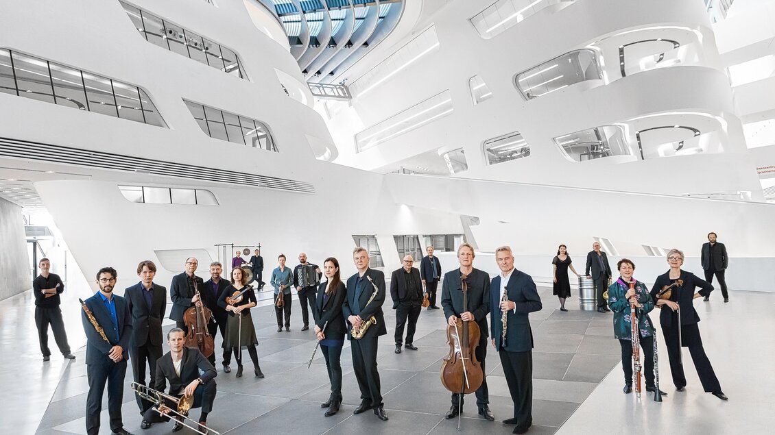 Eine Gruppe von Musikern steht in einem modernen, hellen Raum. Die Architektur ist futuristisch und bietet viel natürliches Licht. | © _c__Tina_Herzl