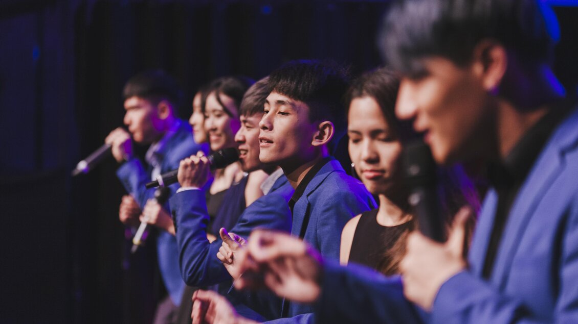 Eine Gruppe von Sängern steht auf der Bühne und präsentiert einen Auftritt. Sie tragen blaue Anzüge und konzentrieren sich auf ihre Darbietung. | © Stefan Lozar