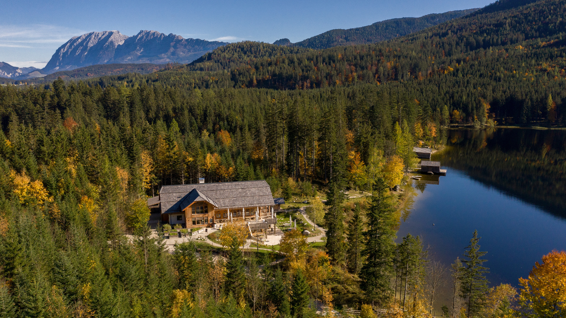 Eine malerische Landschaft mit einem Holzhaus am Ufer eines ruhigen Sees. Im Hintergrund erheben sich majestätische Berge und die Bäume zeigen herbstliche Farben. | © TVB Ausseerland Salzkammergut_Karl Grieshofer