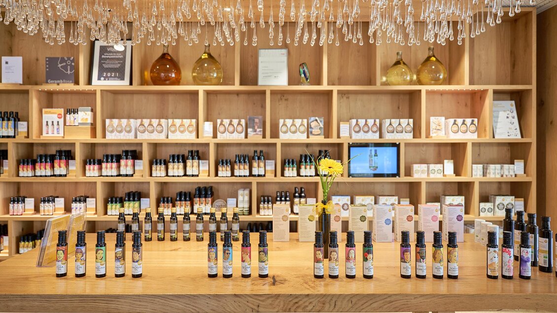 Ein schöner Verkaufsraum mit Holzregalen, die verschiedene Flaschen von Aromatherapieprodukten zeigen. Auf dem Tisch stehen ordentliche Reihen von Sprühflaschen und Blumen dekorieren den Raum. | © Ölmühle Fandler