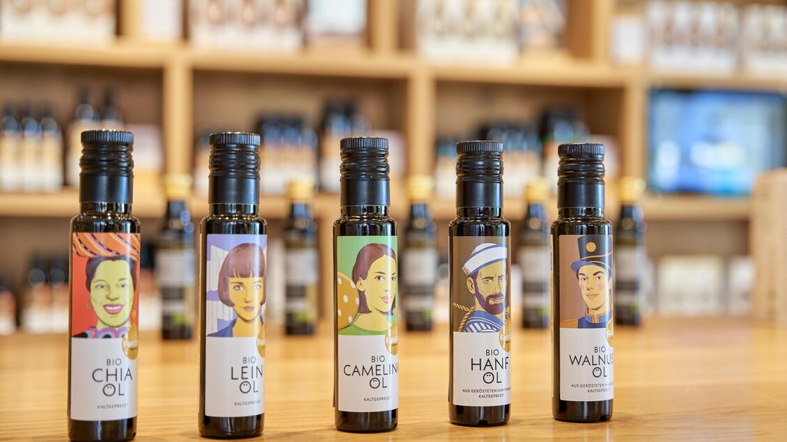 Fünf Flaschen Öl stehen auf einem Holztisch. Jede Flasche hat ein eigenes, farbenfrohes Etikett mit verschiedenen Charakteren. | © Ölmühle Fandler