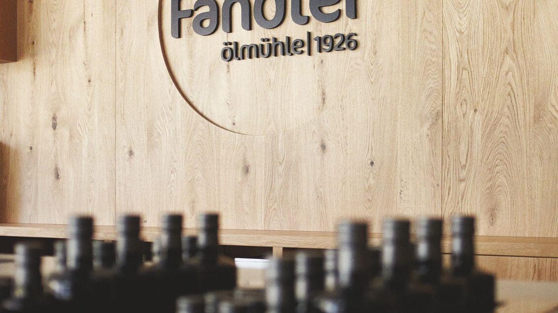 Ein modernes Innendesign mit einer Holzwand und dem Schriftzug "Fandler" ist zu sehen. Im Vordergrund sind feine Details eines Tischs sichtbar. | © Ölmühle Fandler