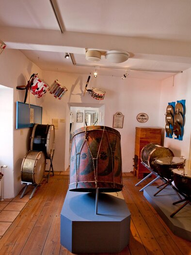 Ein Musikmuseum mit verschiedenen Trommeln und historischen Instrumenten. Die Wände sind mit bunten Fahnen dekoriert. | © Holzwelt Murau