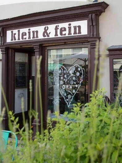 A small, charming shop named "klein & fein" at the storefront.  
In front of the store, green plants grow and there is an inviting atmosphere. | © Weingut Resch vlg. Longus