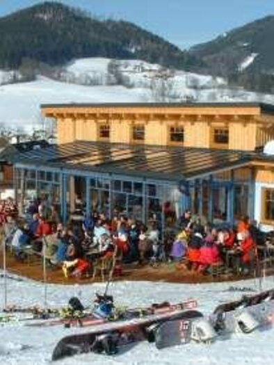 Ein gemütliches Berghaus in den Bergen mit vielen Gästen auf der Terrasse. Umgeben von Schnee und Skiausrüstung genießen die Besucher die Winteratmosphäre. | © TV Hochsteiermark
