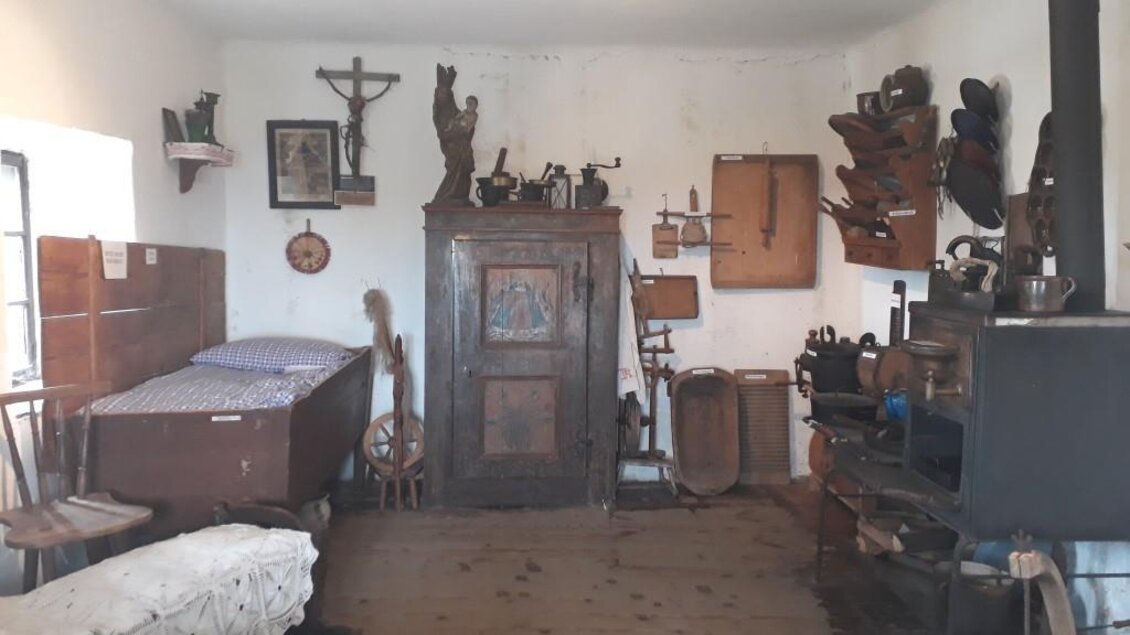 Ein rustikales Zimmer mit einem Bett, einer Holztruhe und verschiedenen alten Möbelstücken. An den Wänden hängen historische Gegenstände und Dekoration. | © TV Südsteiermark