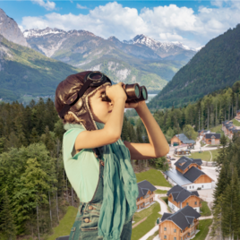 A child wearing aviator glasses looks into the distance with binoculars. In the background, there are mountains and a small, picturesque settlement visible. | © www.zloam.at