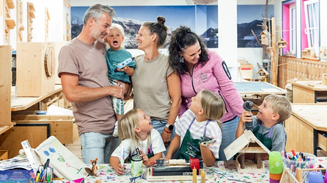 Eine Gruppe von Erwachsenen und Kindern in einem kreativen Werkraum. Sie lachen und arbeiten mit Holz und Bastelmaterialien. | © www.zloam.at