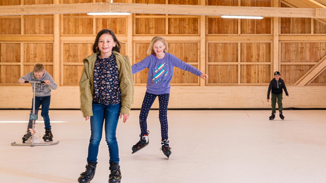 Kinder laufen auf einer Eisfläche. Ein Mädchen skatet fröhlich, während andere in der Nähe spielen. | © www.zloam.at