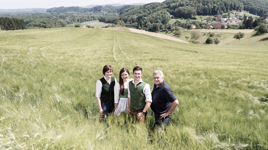 Eine Gruppe von vier Personen steht auf einem grünen Feld mit sanften Hügeln im Hintergrund. Die Szene strahlt ländliche Idylle und Gemeinschaftsgefühl aus. | © Adamarkt Seggauberg