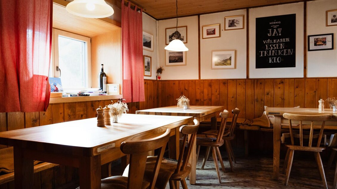 Ein gemütliches Restaurant mit Holztischen und Stühlen. Die Wände sind mit Bildern geschmückt, und rote Vorhänge sorgen für eine einladende Atmosphäre. | © Christoph Lukas