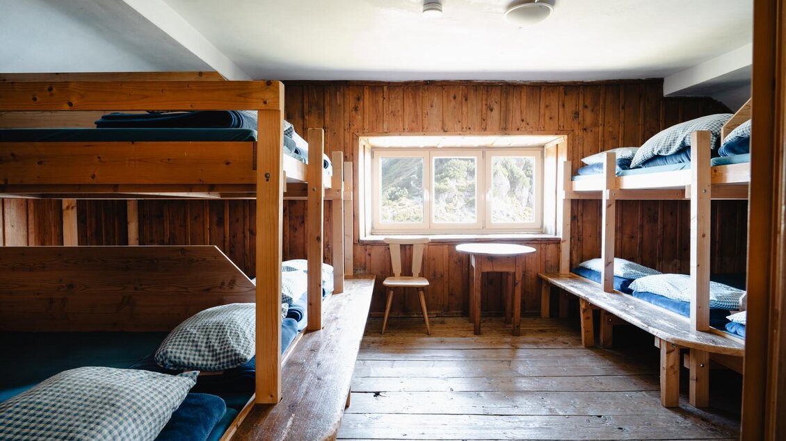 Ein einfaches Zimmer mit Etagenbetten aus Holz. Ein Tisch und Stuhl stehen vor einem Fenster, das Licht hereinlässt. | © Christoph Lukas
