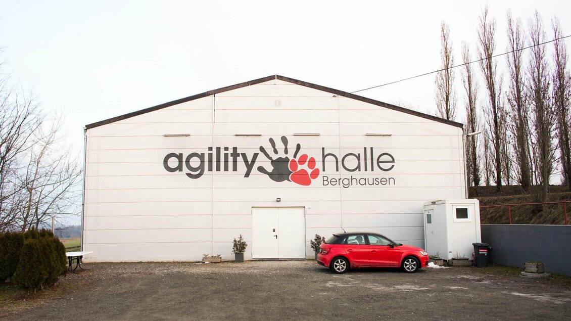 Eine große, weiße Halle mit dem Schriftzug "agility halle Berghausen". Davor steht ein rotes Auto auf einem Schotterplatz. | © Simone Ullrich-Pansi