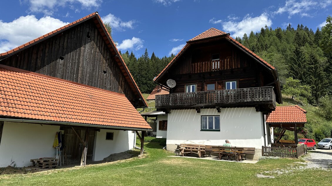 Zwei traditionelle Häuser mit roten Dächern in einer grünen Umgebung. Im Hintergrund sind Berge und ein klarer blauer Himmel zu sehen. | © TV Hochsteiermark