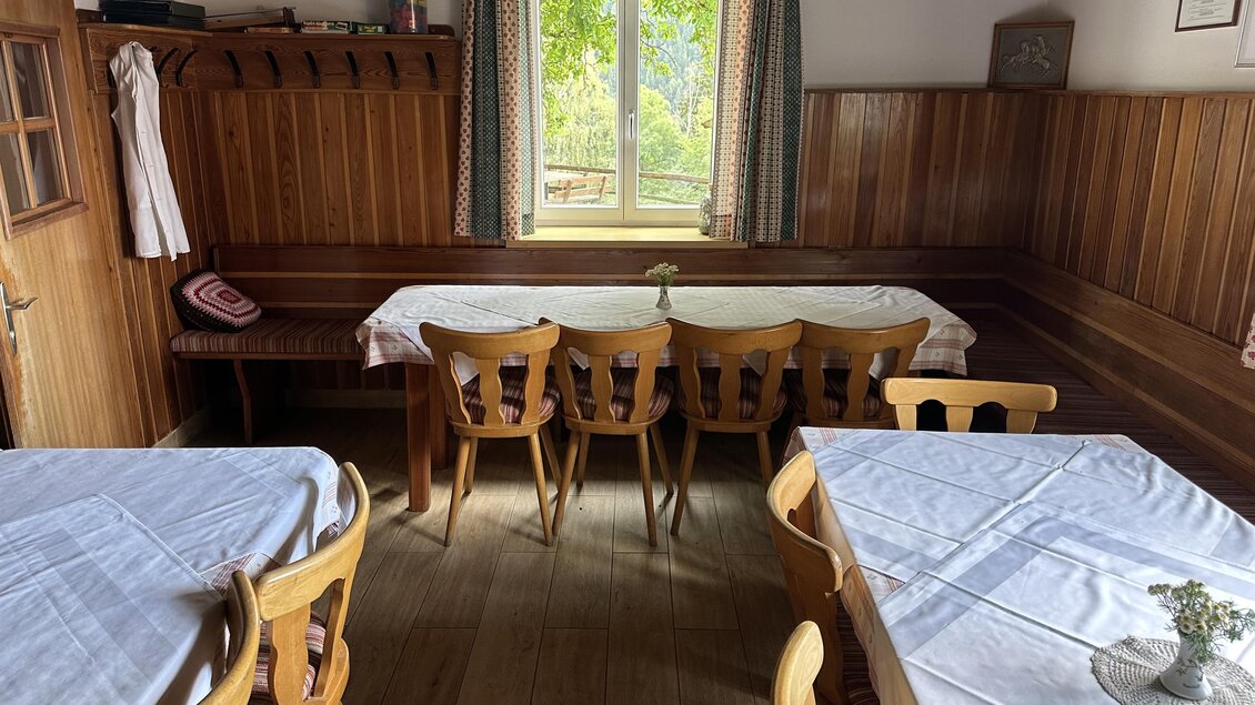 Ein gemütlicher Gastraum mit Holzmöbeln und weißen Tischdecken. Ein Fenster sorgt für viel Tageslicht und einen Blick ins Freie. | © TV Hochsteiermark