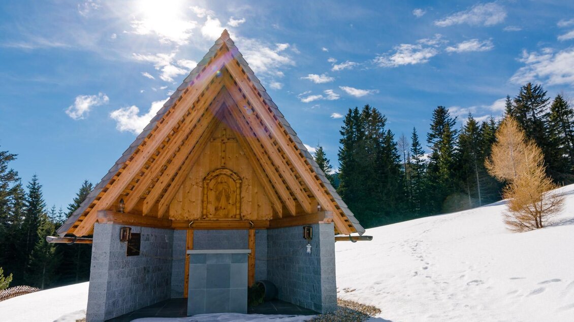 Eine gemütliche Holzhütte im Schnee mit einer schönen Dachkonstruktion. Im Hintergrund sind Bäume und ein blauer Himmel zu sehen. | © Almidylle Sabathy