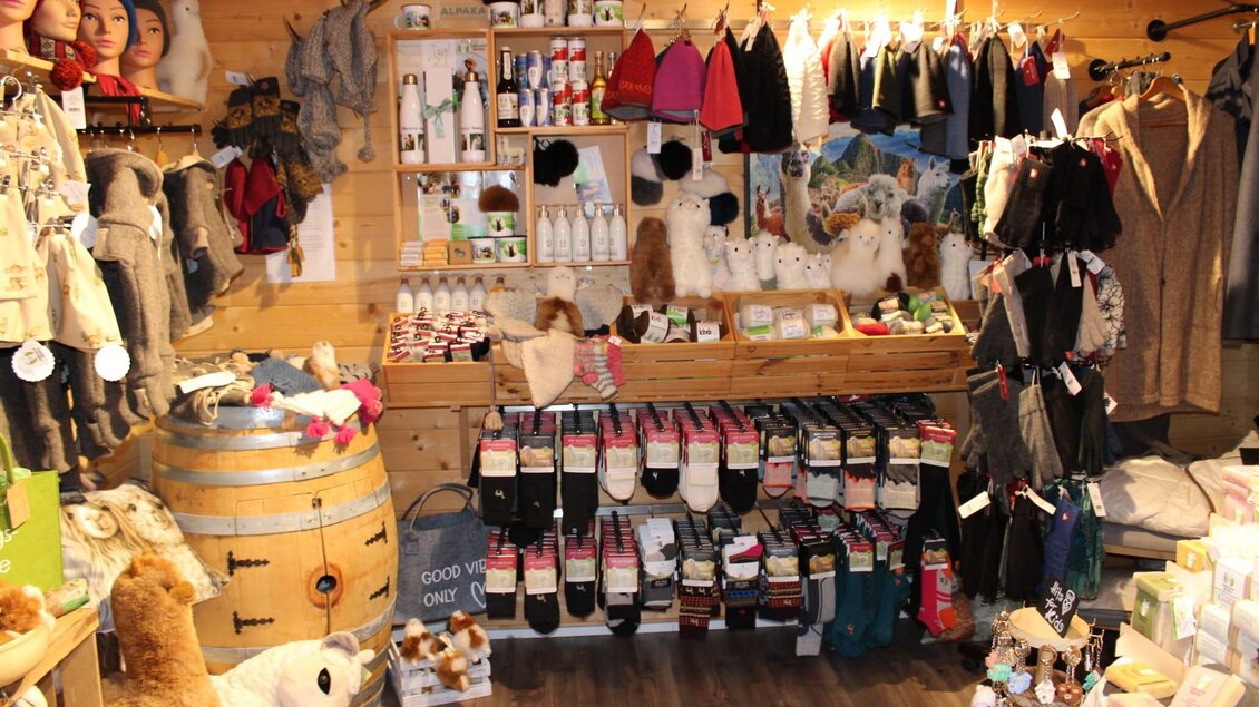 Ein gut ausgestatteter Souvenirladen mit strapazierfähigen handgefertigten Produkten, darunter Wollartikel und kleine Dekorationen. Eine Frau steht lächelnd neben den Regalen. | © Strassegger