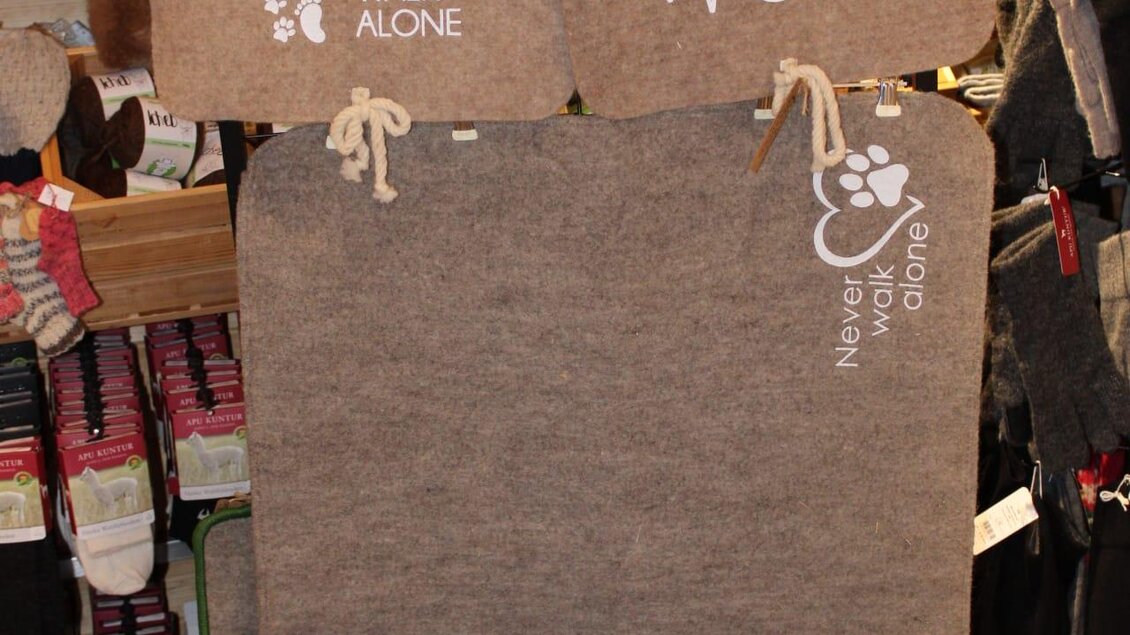 Zwei dekorative Matten hängen im Geschäft. Eine Matte zeigt den Spruch "Ich liebe meine Frau" und die andere hat die Aufschrift "Never walk alone". | © Ganster
