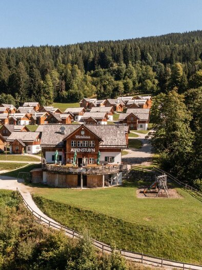 A picturesque landscape with wooden chalets amidst trees. In the foreground, there is a playground and an open area. | © Gerhard Wolkersdorfer