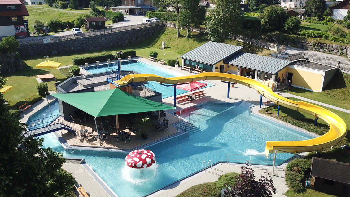 Ein großer Outdoor-Wasserpark mit einem Schwimmbecken, einer Rutsche und einer Lounge. Rund um den Pool gibt es grüne Wiesen und gemütliche Liegestühle. | © Rainer & Steiner GmbH