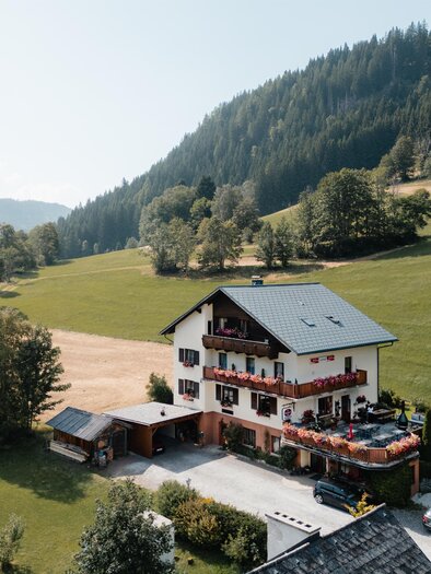 A beautiful building with a balcony, adorned with colorful flowers. In the background, green mountains can be seen. | © TV Gesäuse
