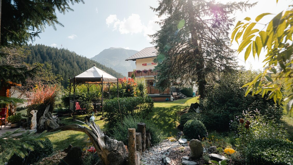 Ein schöner Garten mit Bäumen und bunten Blumen. Im Hintergrund ist ein gemütliches Haus und die Berge zu sehen. | © TV Gesäuse