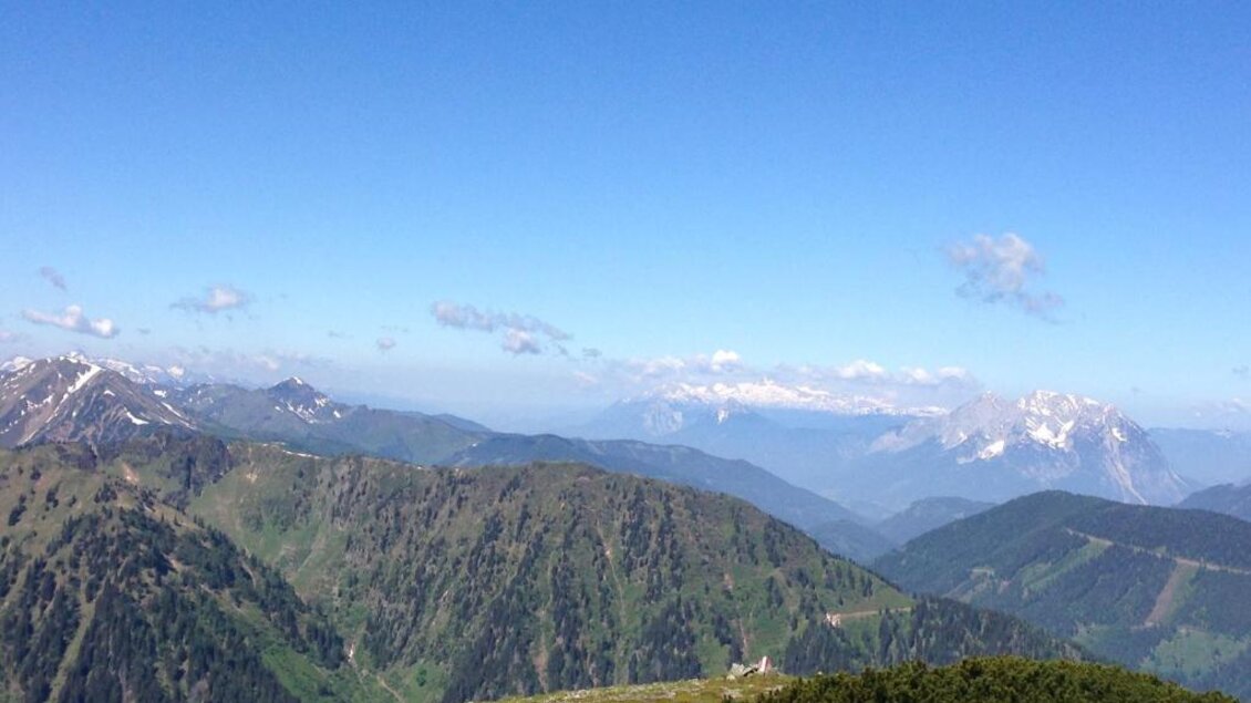 Eine beeindruckende Berglandschaft mit grünen Hügeln und schneebedeckten Gipfeln. Der Himmel ist klar und blau, ideal für Naturliebhaber. | © Grobbauer