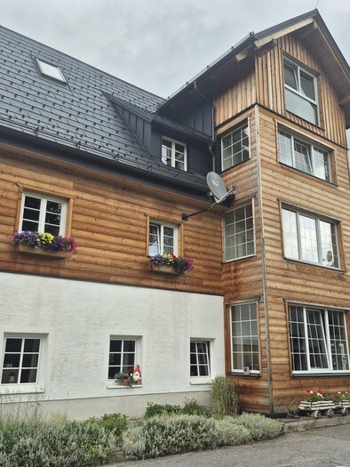 Ein modernes Mehrfamilienhaus mit Holz- und Putzfassade. Es ist von einer grünen Umgebung umgeben und hat große Fenster. | © TV Hochsteiermark