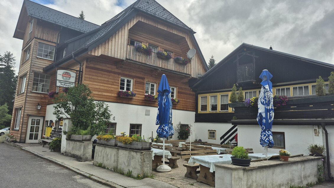 Ein charmantes Holzgebäude mit Blumen und blauen Sonnenschirmen. Die Umgebung ist ruhig und einladend, ideal für einen entspannten Aufenthalt. | © TV Hochsteiermark