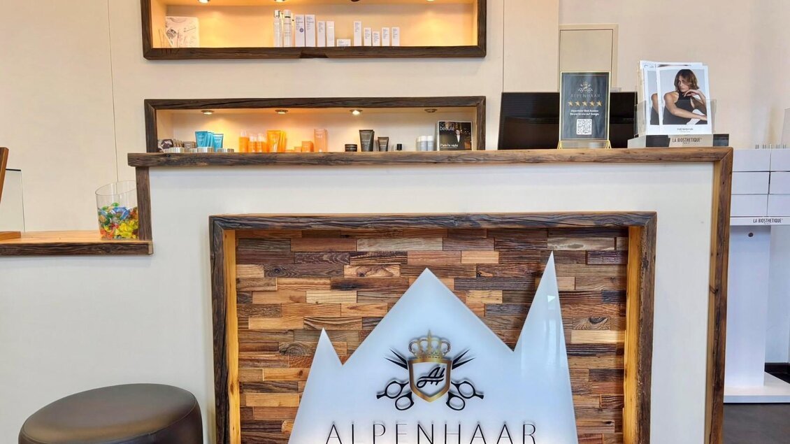 Ein moderner Empfangsbereich mit Holzdetails und Beleuchtung. Das Logo „ALPENHAAR“ ist gut sichtbar und verleiht dem Raum eine einladende Atmosphäre. | © Alpenhaar Bad Aussee