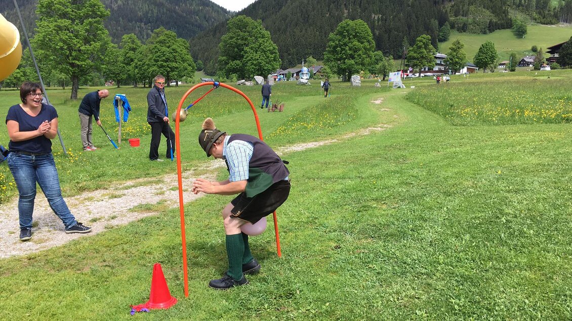 Ein Fest im Freien mit mehreren Menschen, die an einem Wettkampf teilnehmen. Im Vordergrund springt ein Teilnehmer durch einen roten Bogen. | © Alpincenter Dachstein