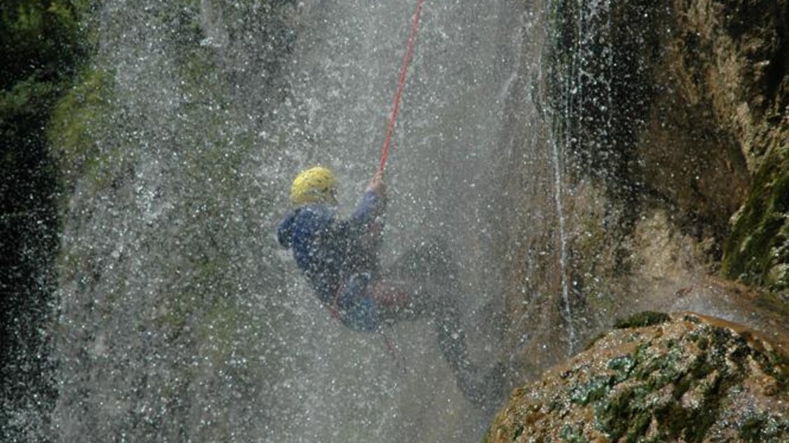 Eine Person klettert an einem Wasserfall hinunter. Sie ist mit einem Klettergeschirr und einem Helm ausgestattet. | © Alpincenter Dachstein