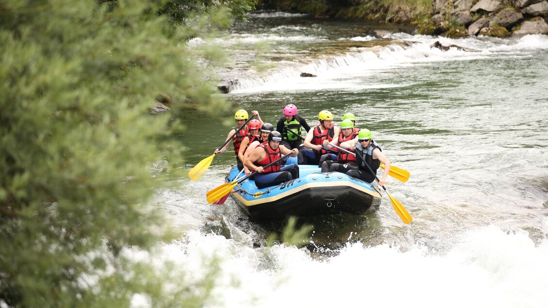 Eine Gruppe von Menschen paddelt in einem Raft auf einem reißenden Fluss. Sie tragen Schwimmwesten und Helme und scheinen viel Spaß zu haben. | © Alpincenter Dachstein