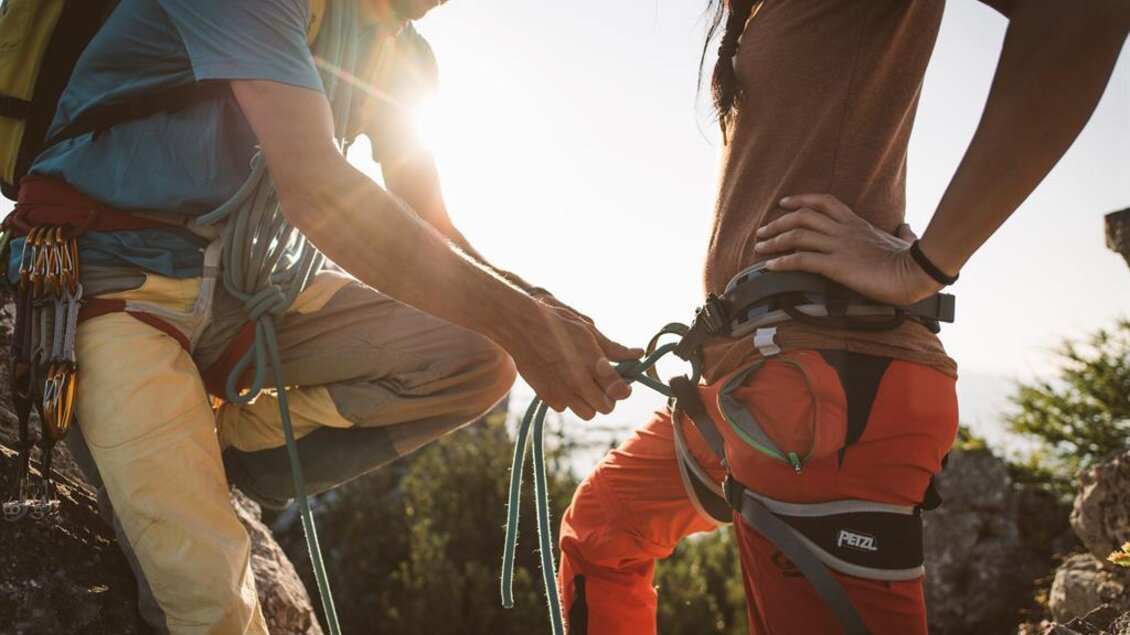 Ein Kletterer sichert eine Kletterpartnerin mit einem Karabiner. Im Hintergrund ist die Sonne zu sehen, die eine warme Atmosphäre schafft. | © Stefan Leitner