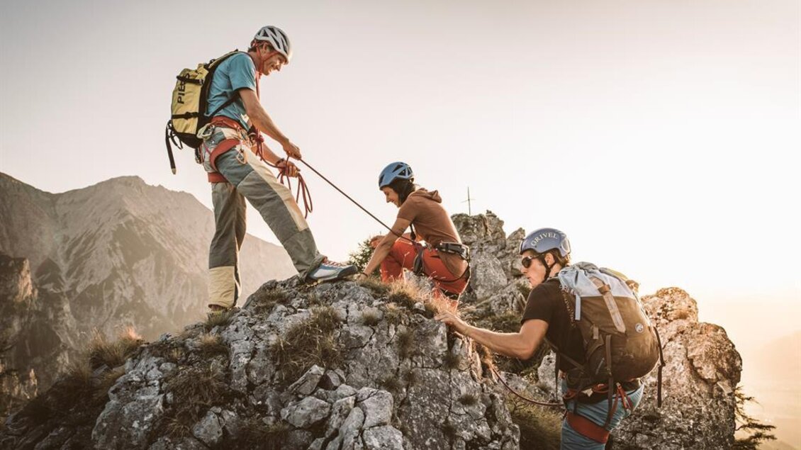 Drei Bergsteiger sichern sich gegenseitig beim Klettern auf einem Felsen. Die Sonne scheint und die Umgebung ist beeindruckend. | © Stefan Leitner