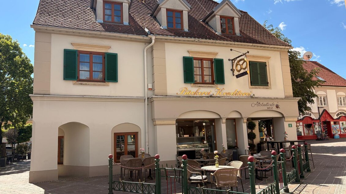 Eine charmante Bäckerei in einer kleinen Stadt mit Außenplätzen und Sonnenschirmen. Die Gebäude zeigen traditionelle Architektur und laden zum Verweilen ein. | © Oststeiermark Tourismus