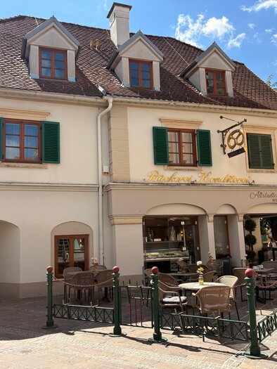 A charming bakery in a small town with outdoor seating and sun umbrellas. The buildings showcase traditional architecture and invite you to linger. | © Oststeiermark Tourismus