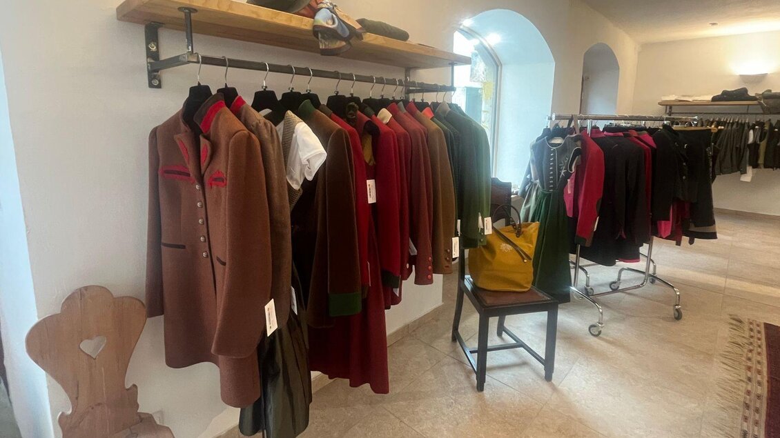 Ein Verkaufsraum mit traditionellen Kleidungsstücken an Kleiderständern. Die Kleidung ist hauptsächlich in rustikalen Farbtönen gehalten, und es gibt einige Accessoires auf einem Tisch. | © TVB Ausseerland Salzkammergut_Nathalie Schröttenhamer
