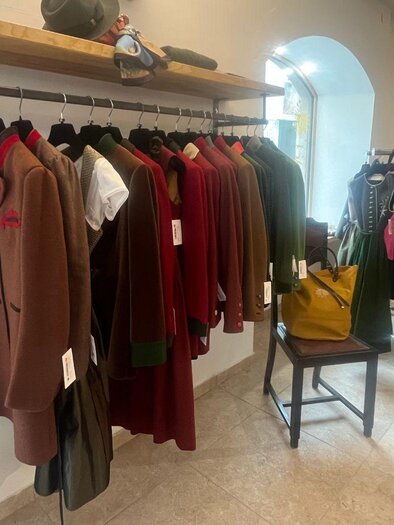 A sales room with traditional garments on clothing racks. The clothing is mainly in rustic color tones, and there are some accessories on a table. | © TVB Ausseerland Salzkammergut_Nathalie Schröttenhamer