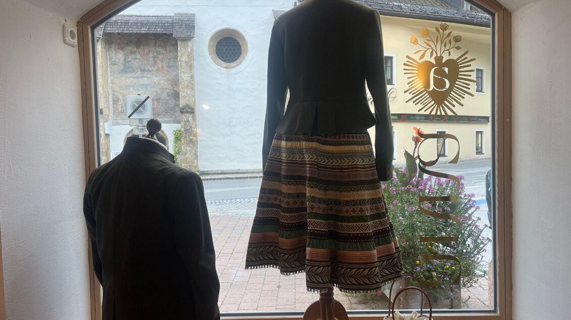 Ein Schaufenster mit einem traditionellen Kleid und einem Jackett. Im Hintergrund sieht man die Straße und ein dekoratives Element. | © TVB Ausseerland Salzkammergut_Nathalie Schröttenhamer