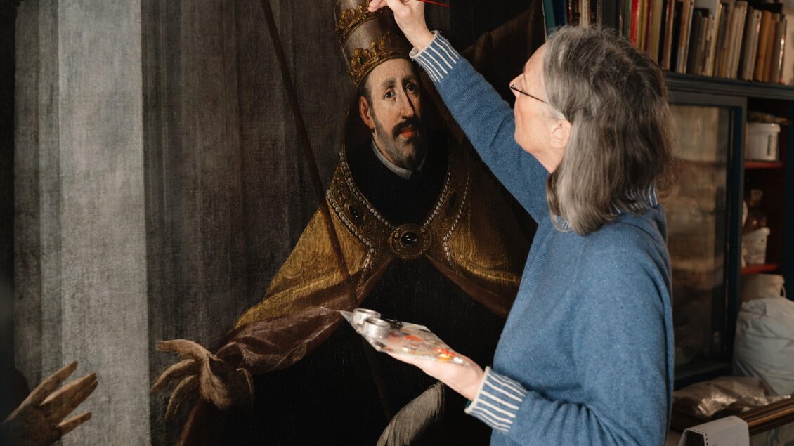 Restauratorin Erika Thümmel arbeitet mit Pinsel und Palette an einem historischen Porträtgemälde in ihrem Atelier in Graz. | © Bernd Grosseck